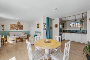 Ein modernes Wohnzimmer mit einer Couch, einem Esstisch und Stühlen. Es gibt eine Küchenzeile mit Schränken und einem Fenster.