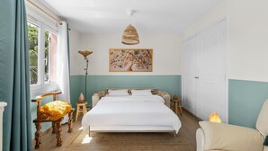 Une chambre à coucher avec un lit, une table de chevet, une lampe, une chaise, une fenêtre avec des rideaux et un tableau au mur.