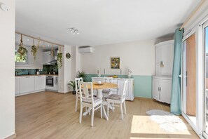 Eine Küche mit weißen Schränken, einem Esstisch mit Stühlen, hängenden Pflanzen und einem Bild an der Wand.