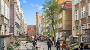 A cobblestone street lined with historic buildings, a prominent tower, and a market area with stalls. - Leśna Aura by Grand Apartments (Sopot)