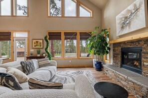 Ein geräumiges Wohnzimmer mit Kamin, großen Fenstern und einem gemütlichen Sofa.