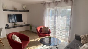 A modern living room with a flat-screen TV, red armchairs, a round coffee table, and a grey sofa. - Modern apartment with sea view in the old town of Crikvenica (Crikvenica)