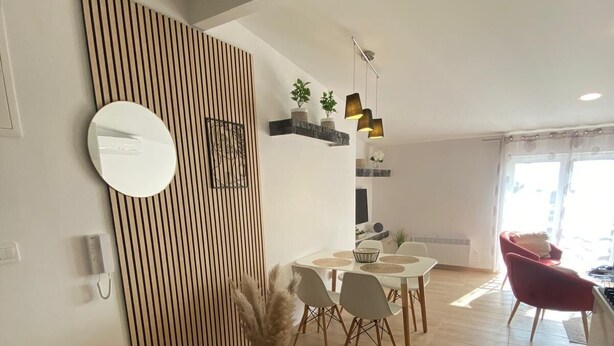 A modern dining area with a wooden slat wall, a round mirror, and a dining table with chairs. - Modern apartment with sea view in the old town of Crikvenica (Crikvenica)
