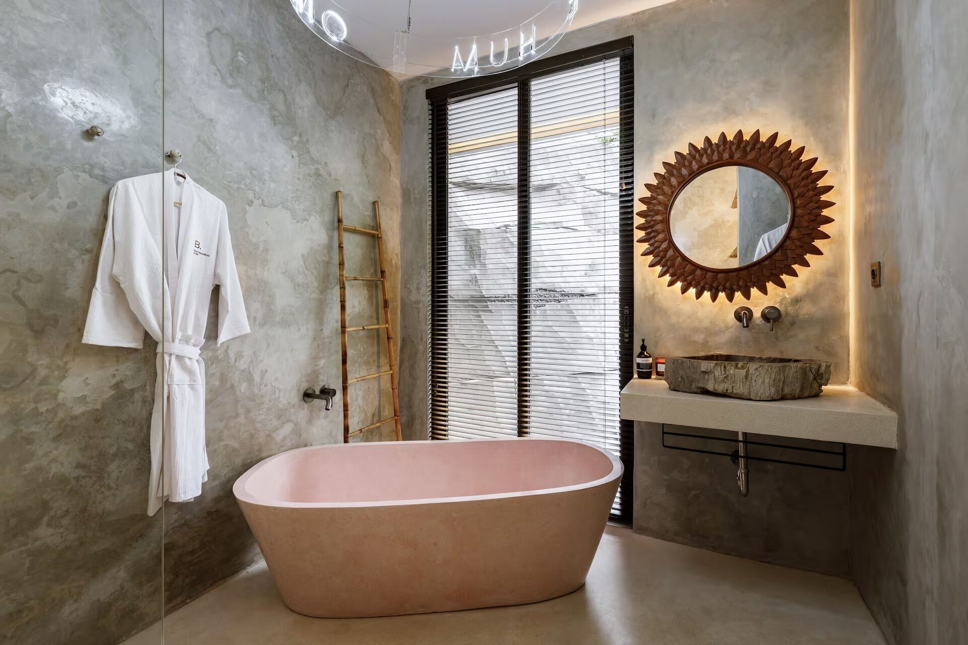 A bathroom with a freestanding bathtub, a vanity with a sunburst mirror, and a towel rack with a white robe.
