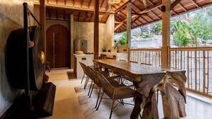 Uma área de refeições com mesa e cadeiras de madeira, cozinha ao fundo e vista para o verde lá fora.