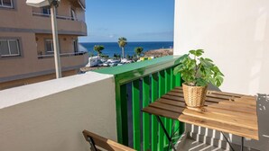 A balcony with a wooden table, a potted plant, and a view of the ocean and buildings. - Vacation Home 'Los Abrigos Sea View' with Ocean Views, Balcony and Wi-Fi (Los Abrigos)