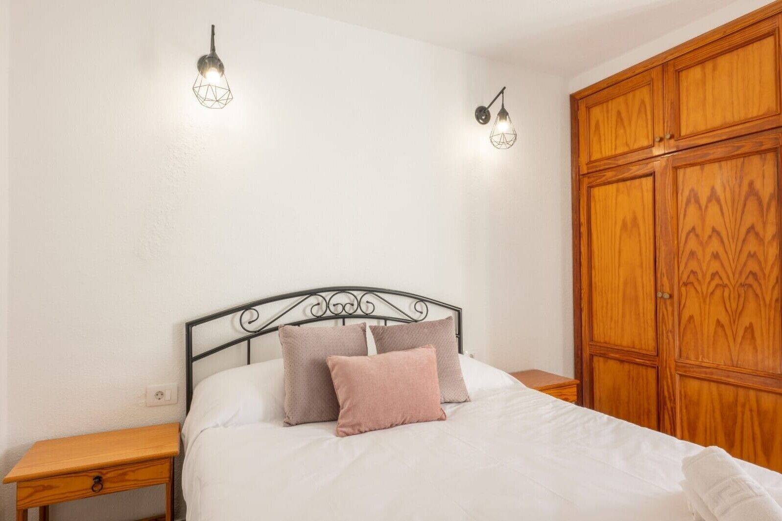 Un dormitorio con una cama, dos luces empotradas en la pared, un armario de madera y una mesita de noche.