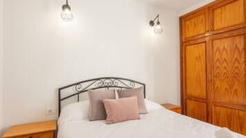 Un dormitorio con una cama, dos luces empotradas en la pared, un armario de madera y una mesita de noche.