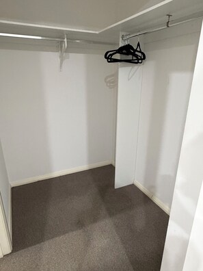 Huoneessa on harmaa matto, valkoiset seinät ja katosta roikkuva vaateteline.