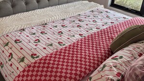 Ein Schlafzimmer mit einem großen Bett, einem grauen, gepolsterten Kopfteil und Blick auf die Straße durch ein Fenster.