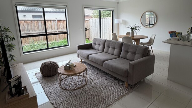 Ein modernes Wohnzimmer mit einem grauen Sofa, einem runden Couchtisch und einem großen Fenster.