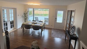 En matplats med ett bord dukat för fyra personer, en krukväxt och utsikt över trädgården genom en glasdörr.