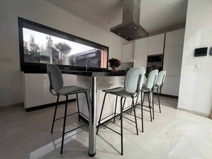 Een moderne keuken met een groot raam, een eettafel met stoelen en een inbouwoven.