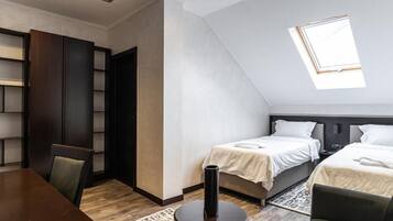 A room with two beds, a dining table, and a bookshelf.