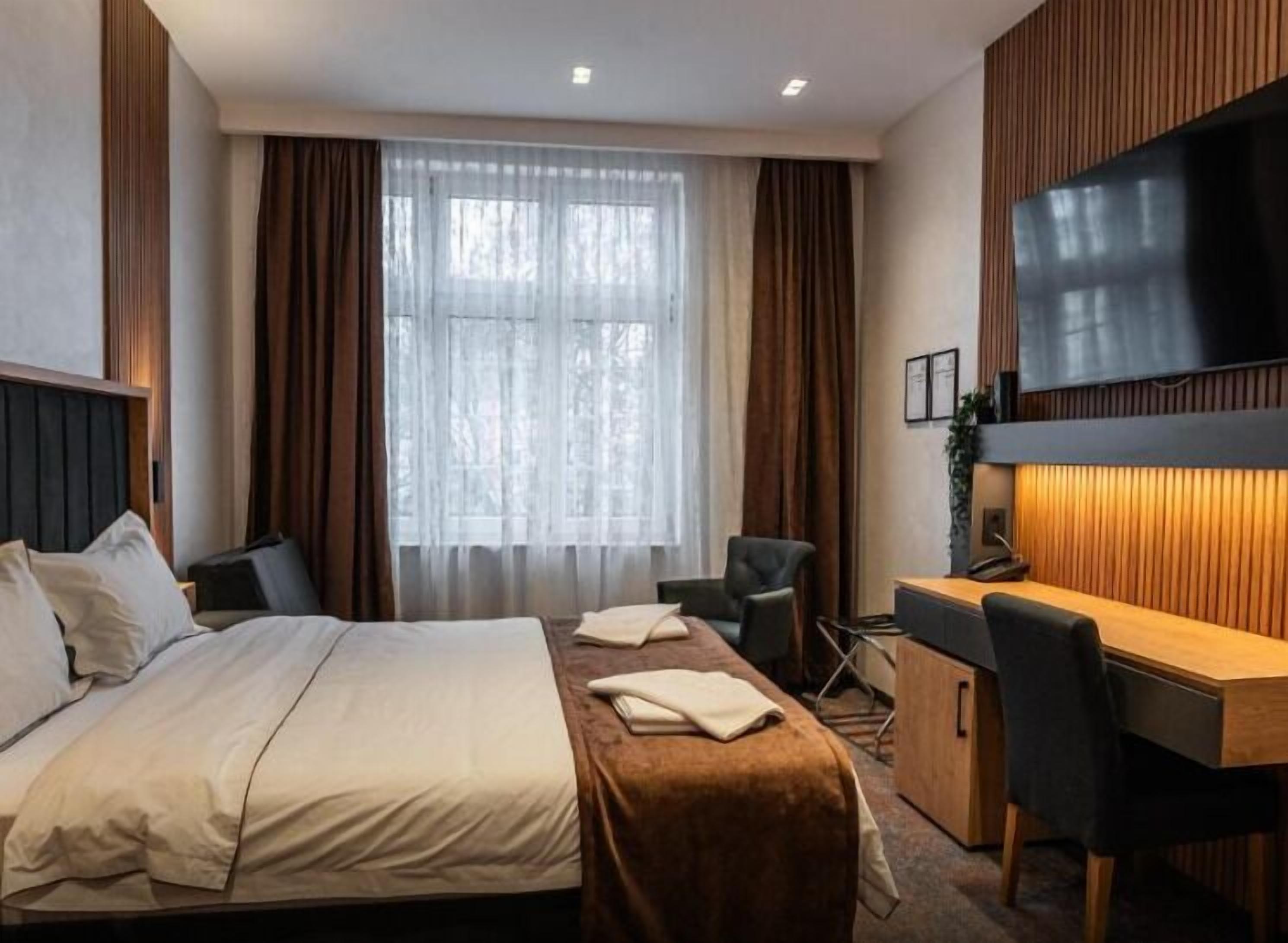 A hotel room with a bed, desk, chair, TV, and curtains.