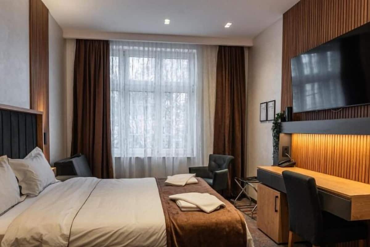 A hotel room with a bed, desk, chair, TV, and curtains.