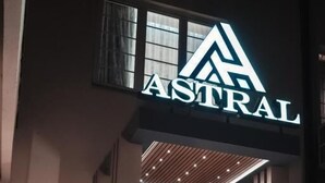 Un hall d'hôtel avec une enseigne indiquant « ASTRAL », un comptoir d'accueil, un escalier et un ventilateur.