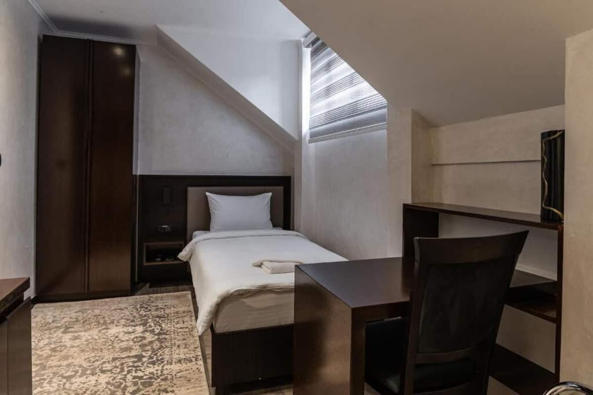 Habitación de hotel pequeña con cama, escritorio, silla, armario y tragaluz.