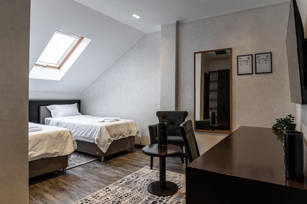 A bedroom with two beds, a desk, a chair, a mirror, and a skylight.