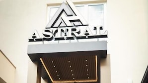 A hotel entrance with a sign reading 'ASTRAL,' a man holding a suitcase, and a woman standing beside him. - Hotel Astral (Šabac)