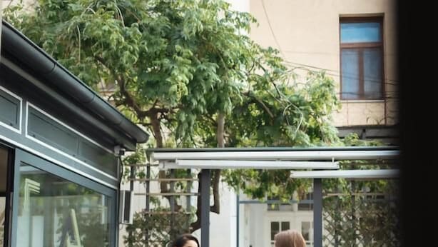 Two people walking on a patio with outdoor seating and a building in the background. - Hotel Astral (Šabac)