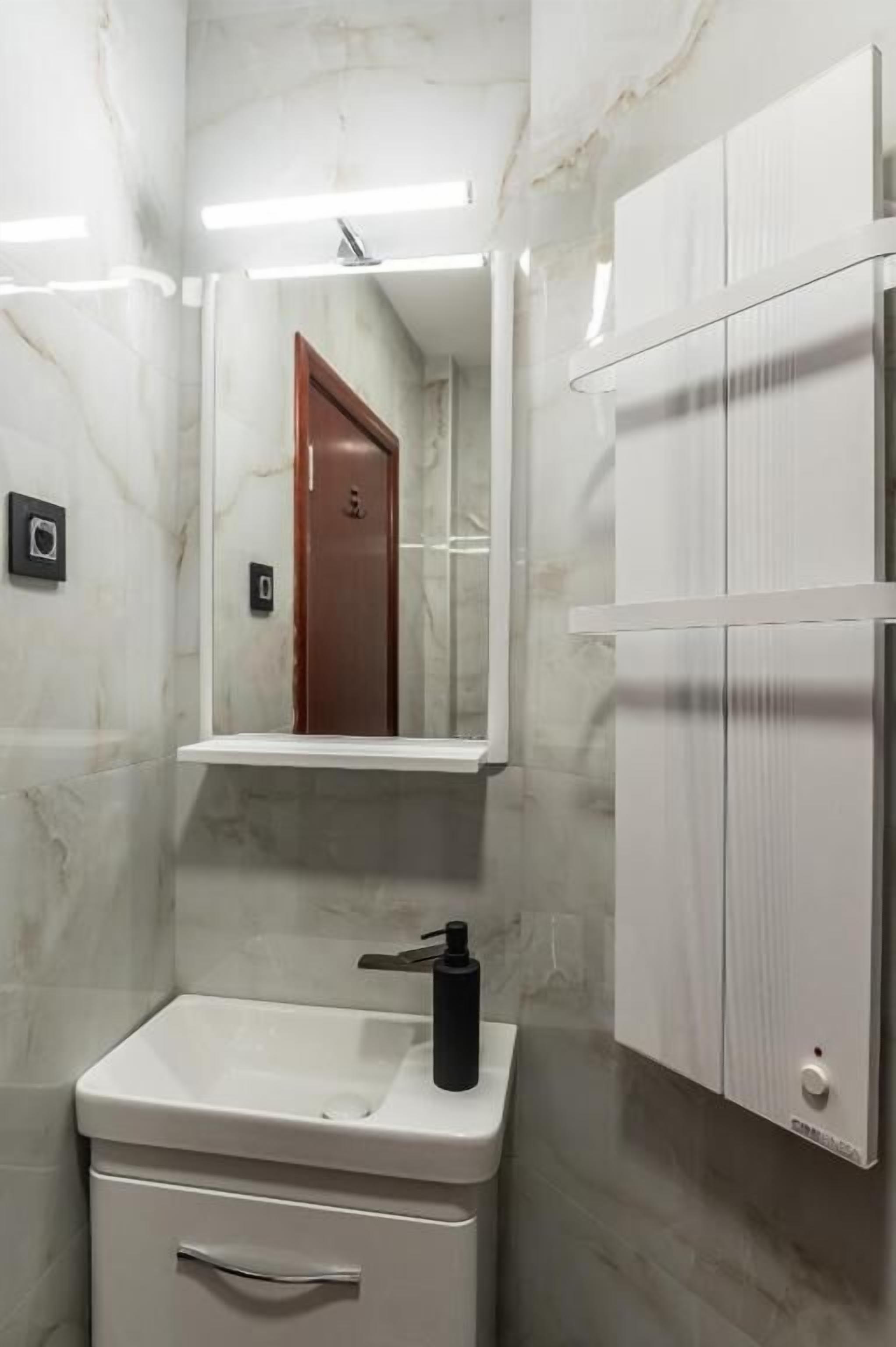A bathroom with a marble wall, a white sink, a mirror, and a door.
