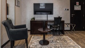 A modern room with a sofa, a desk, a chair, a TV mounted on the wall, and a patterned rug. - Hotel Astral (Šabac)