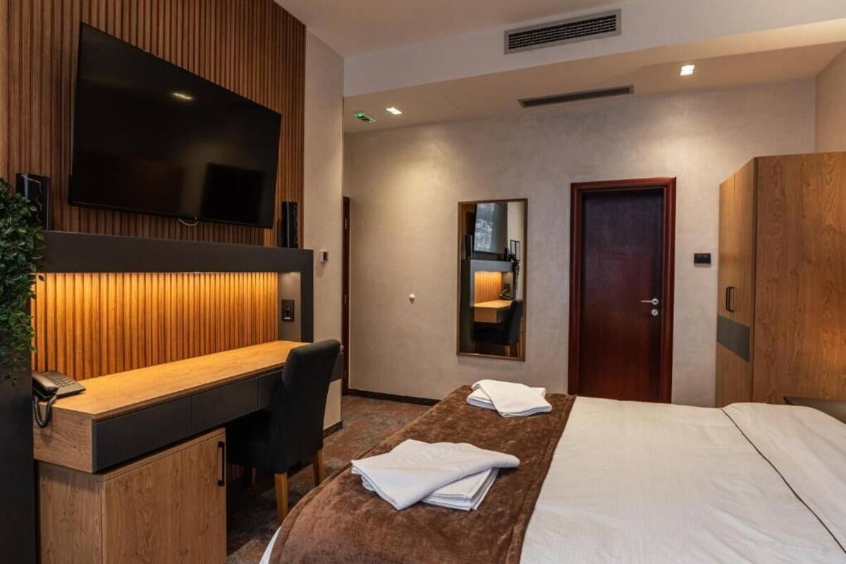 Habitación de hotel con cama, escritorio con teléfono, televisor montado en la pared, espejo y puerta.