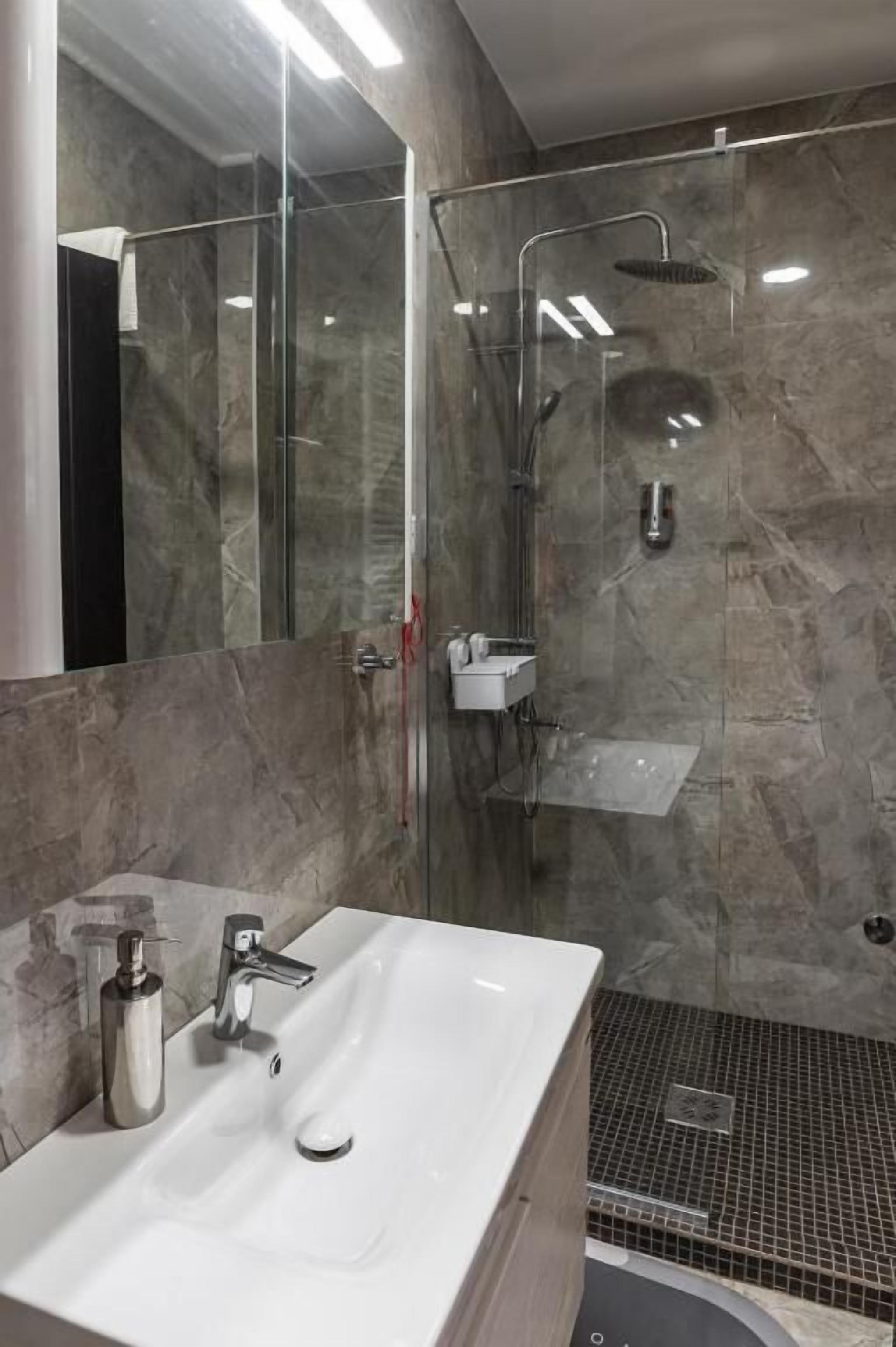 A modern bathroom with a glass-enclosed shower, a white sink, and a mirror.