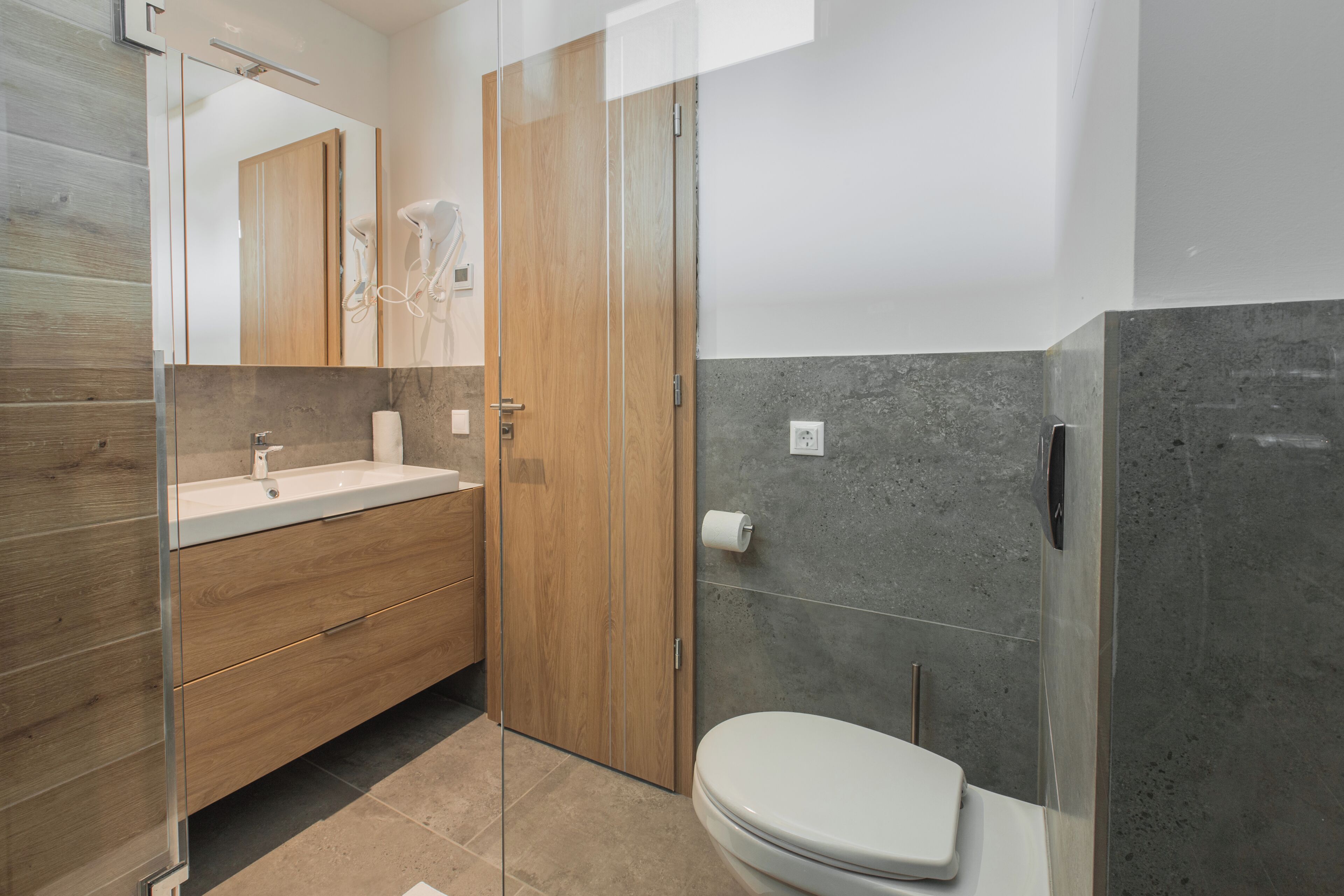 A modern bathroom with a wooden vanity, a glass shower enclosure, and a toilet.