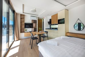Una habitación de hotel moderna con una cama, un escritorio, una kitchenette y un ventanal grande.