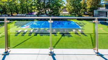 Una piscina con barandilla de vidrio, rodeada de césped cuidado y árboles.