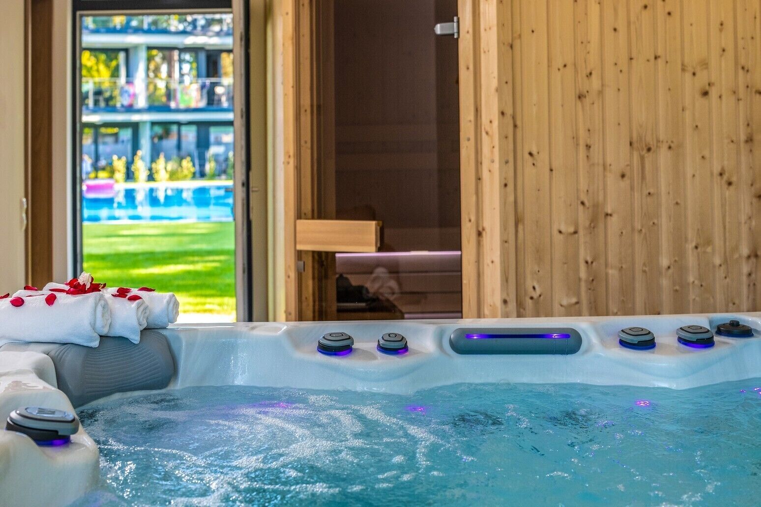 Un jacuzzi con controles, una toalla con pétalos de rosa y vistas a un paisaje verde a través de una puerta abierta.