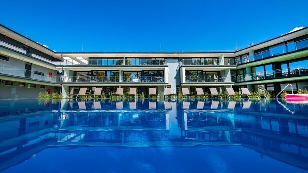 Un hotel moderno con una piscina central, varios balcones y un cielo azul despejado.