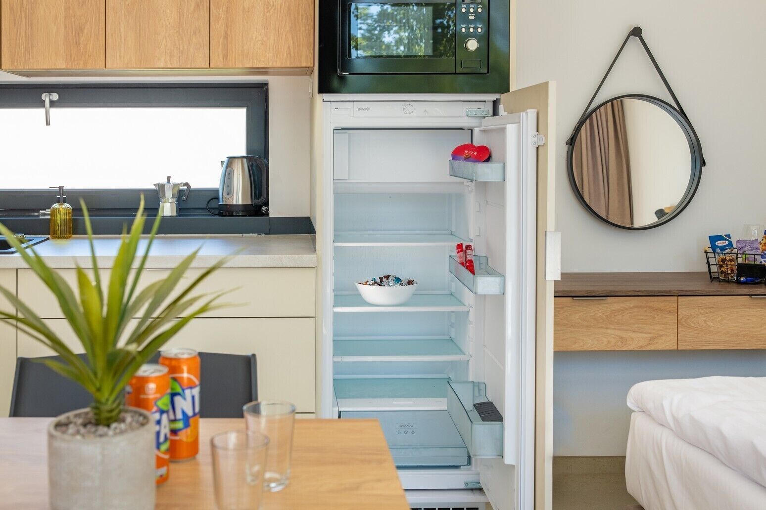 A compact kitchen with a microwave, a refrigerator with a bowl of items, a small potted plant, and a window.