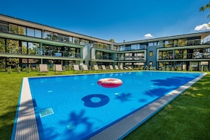 Un hôtel moderne doté d’une piscine, de chaises longues et offrant une vue sur un ciel d’un bleu éclatant.
