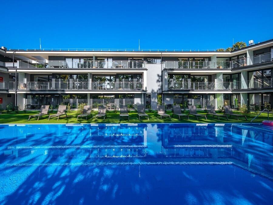 A modern hotel with a central swimming pool, multiple balconies, and a well-maintained lawn.