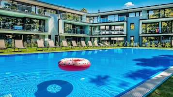 A modern hotel with a swimming pool, lounge chairs, and a clear blue sky.
