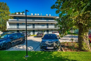 A multi-story building with a parking area, cars, and a tree. - H55 Apartmanházak (Balatonlelle)