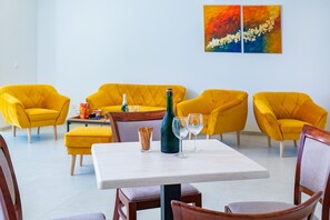 A room with yellow armchairs, a white table with a bottle and glasses, and a painting on the wall. - H55 Apartmanházak (Balatonlelle)
