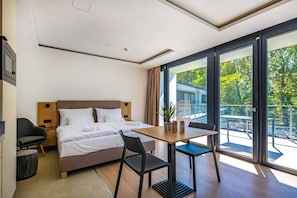 Une chambre d’hôtel comprenant un lit, un bureau, une chaise, une plante en pot et un balcon avec une rambarde.