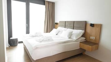 Un hotel moderno con una cama grande, una mesita de noche de madera, un otoman gris y vistas al exterior.