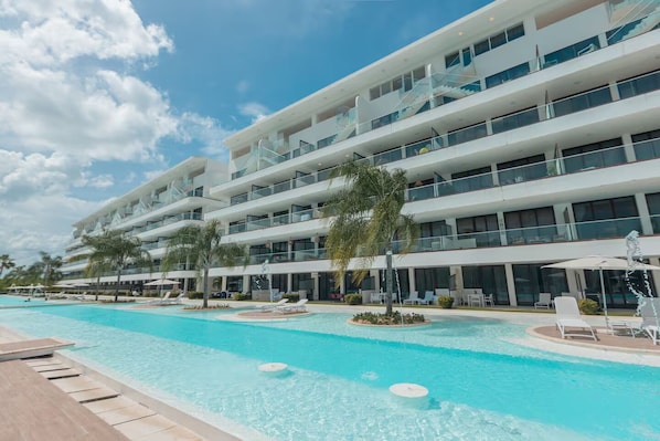 Ein mehrstöckiges Hotel mit Schwimmbad, Sitzgelegenheiten im Freien und Palmen.