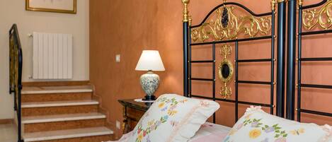 Um quarto com uma cama, uma mesa de cabeceira com abajur, um quadro na parede e uma escada.