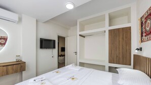 A hotel room with a bed, a TV, a wooden shelf, and a wardrobe.