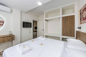 Quarto de hotel com cama, televisão, aparador de madeira e guarda-roupa.