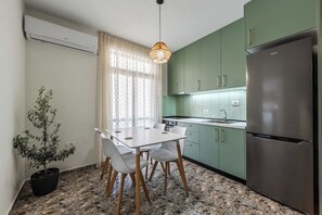 Uma cozinha compacta com mesa, cadeiras, geladeira e um vaso de planta.
