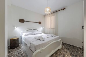 Une chambre à coucher avec un lit, une table de chevet, un luminaire suspendu et une fenêtre avec des rideaux.