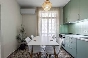 Une cuisine compacte comprenant une table à manger, des chaises, un luminaire suspendu et une plante en pot.