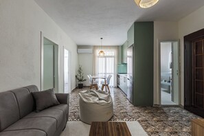 Un salon moderne comprenant un canapé, une table basse, un coin repas avec des chaises, une cuisine avec des placards et une salle de bain visible à travers une porte ouverte.